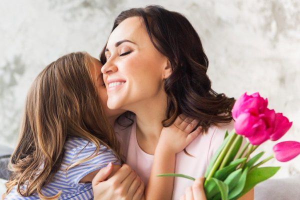 Mother and Little girl embrace over Mother's Day Bouquet. 